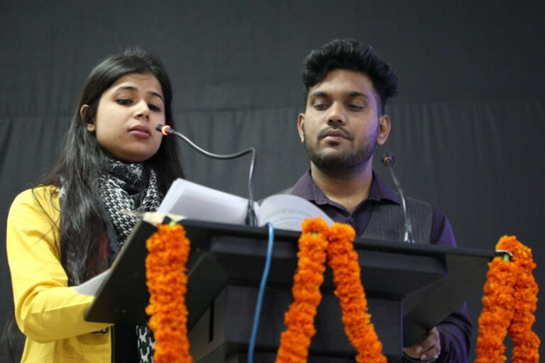 Two students speaking together from a decorated lectern at an ISM Ranchi event